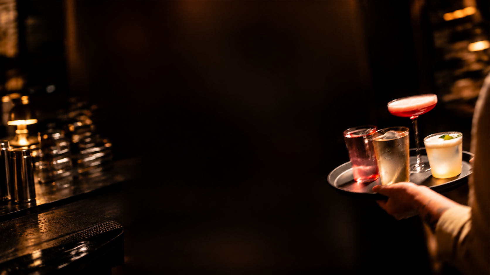 A bartender carrying a tray of cocktails through a dimly lit bar